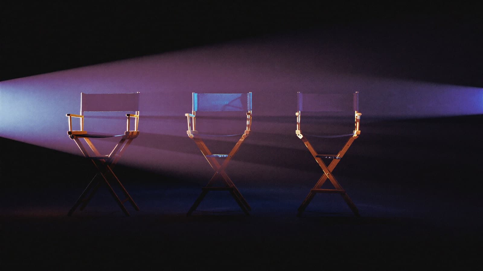 Three director chairs under three spotlights on a dark stage